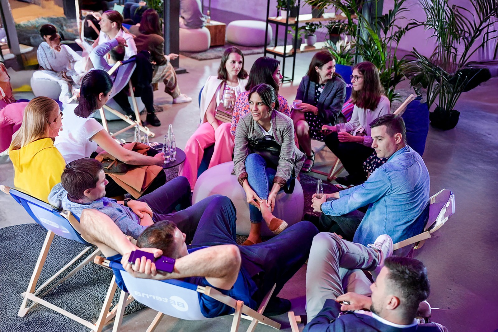 Young IT professionals networking at BE-terna career event in modern coworking space with casual seating and vibrant atmosphere.